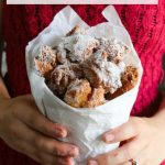 Woman in red sweater holding paper cone of zeppole (fried Italian donuts)