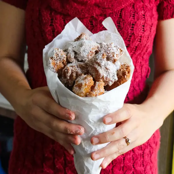 Woman in red sweater holding paper cone full of zeppole (fried Italian donuts)