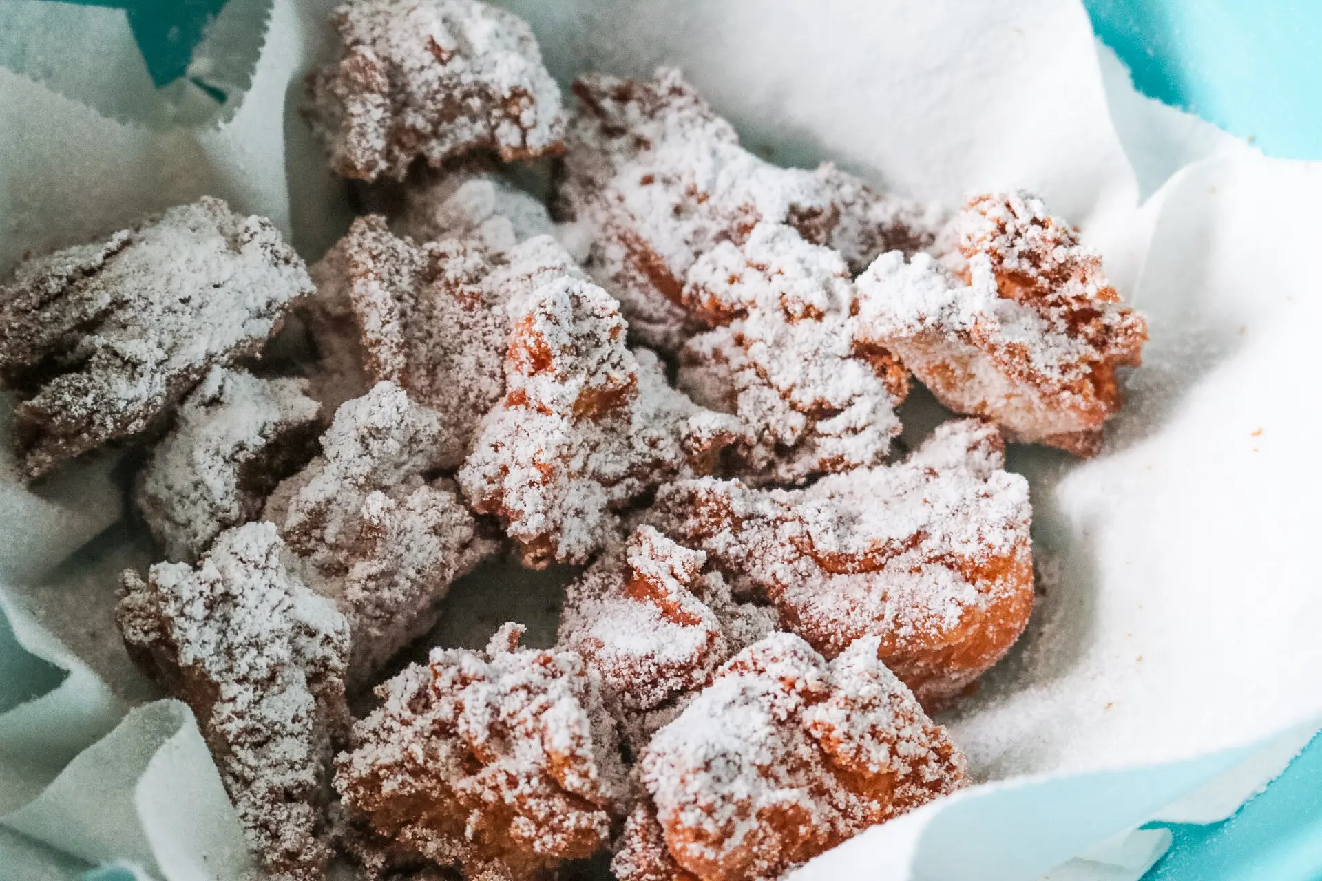 Zeppole (fried Italian donuts) coated in powdered sugar in bowl with paper towels