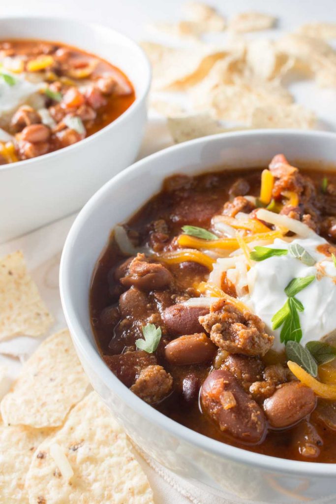 Closeup side view of easy turkey chili in white bowl topped with sour cream, surrounded by tortilla chips