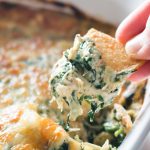 Closeup of baked spinach, artichoke, and crab dip scooped onto a pita chip