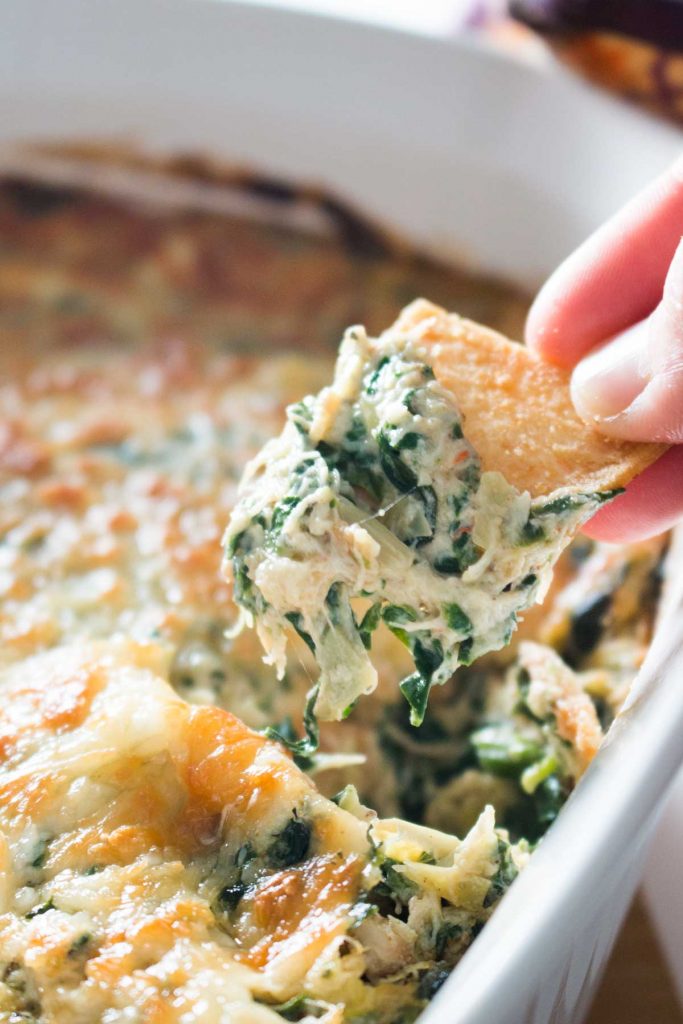 Closeup of pita chip scooping baked spinach, artichoke, and crab dip