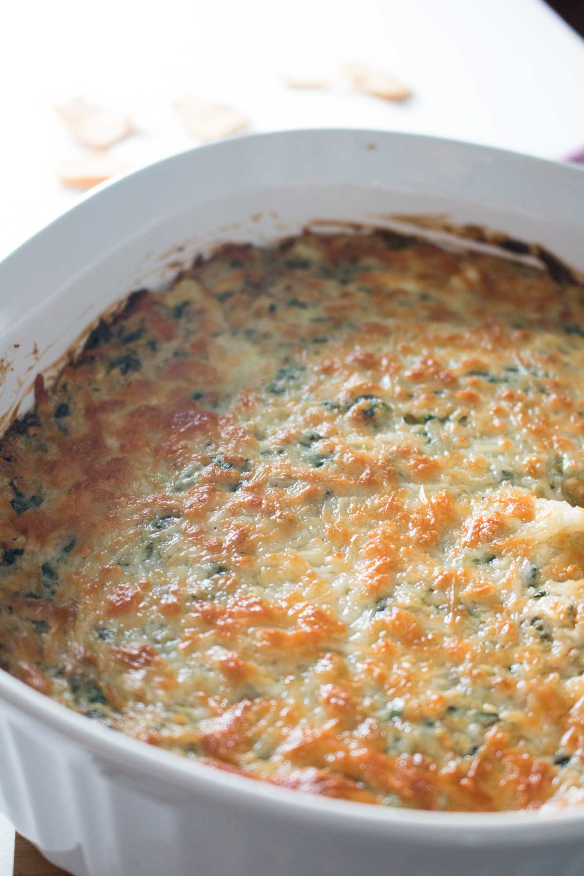 Closeup of bubbly brown cheese on top of baked spinach, artichoke, and crab dip in white casserole dish