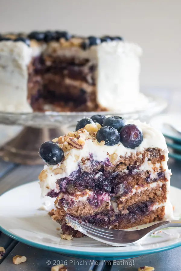 Blueberry spice cake with walnuts is layered with gooey blueberry jam and cream cheese frosting, and topped with walnuts and fresh berries for the perfect bite. A great cake for spring! | www.pinchmeimeating.com