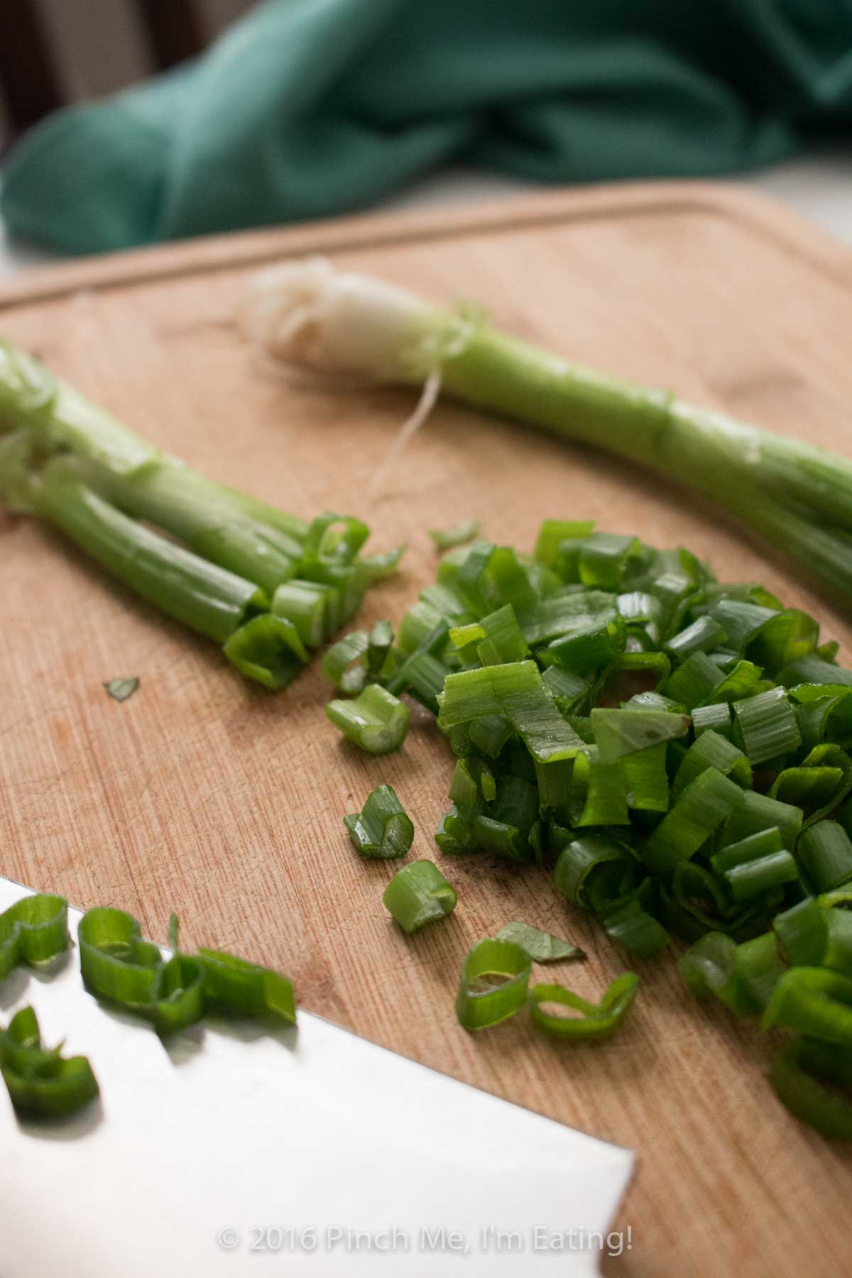 Thinly sliced green onions on a wooden cutting board.