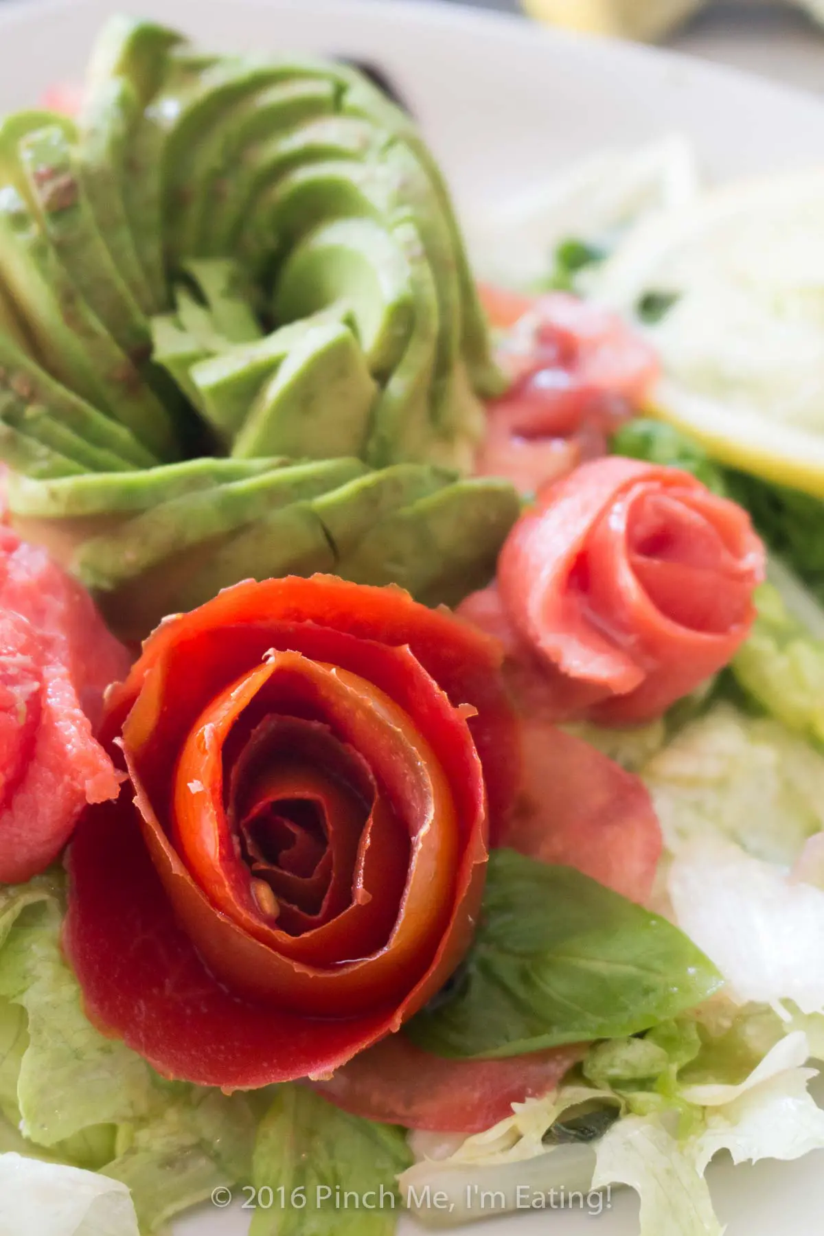 Smoked salmon, tomato, and avocado roses with salad on a white plate.