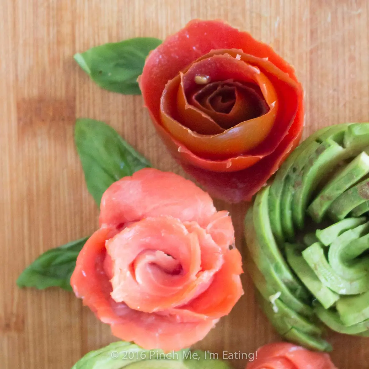Edible smoked salmon, tomato, and avocado roses on a wooden cutting board.