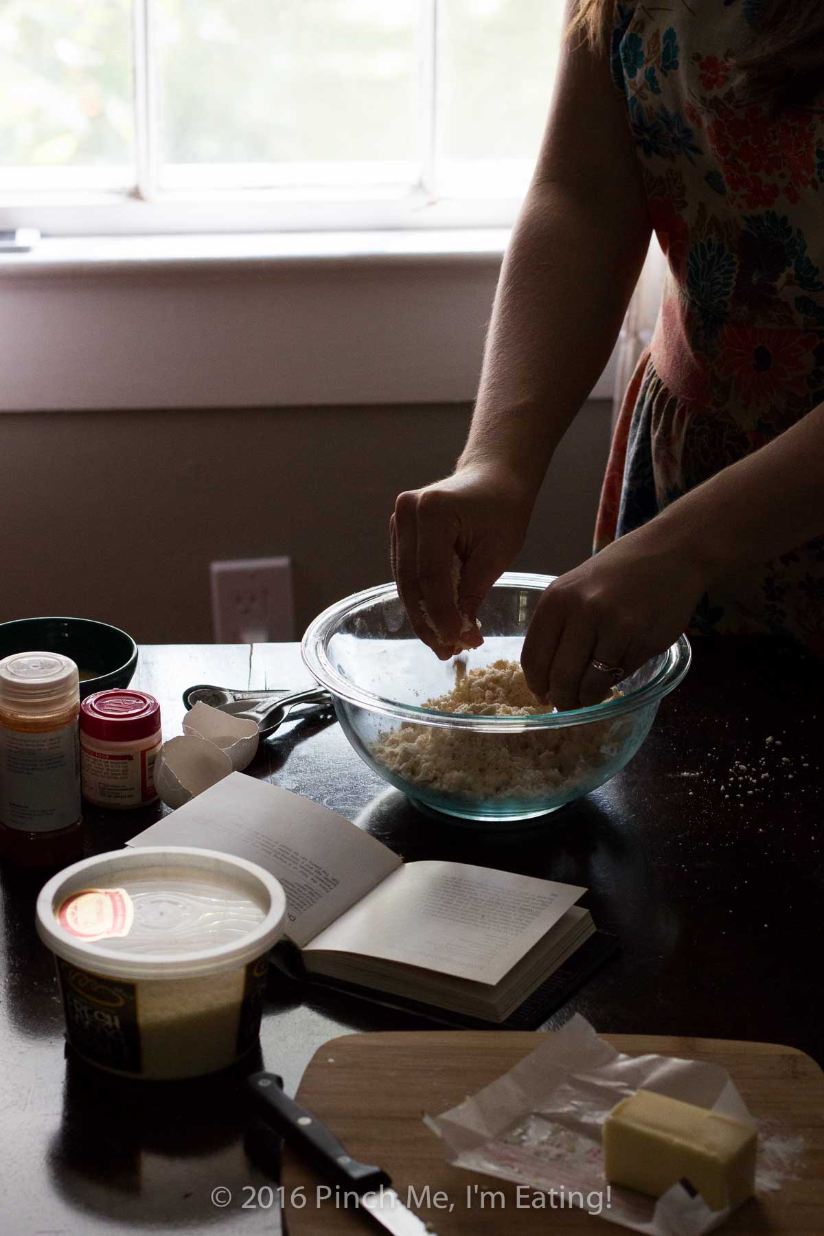 Moody photo of woman making homemade pastry dough in a glass bowl.