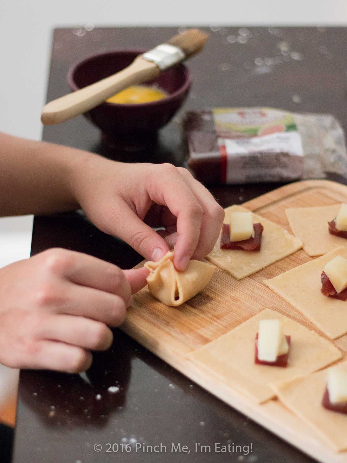 Hands pinching together corners of small pastry squares into a dumpling shape.