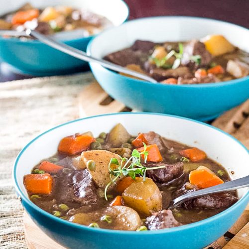 Beef stew with carrots, potatoes, and red wine in three blue bowls