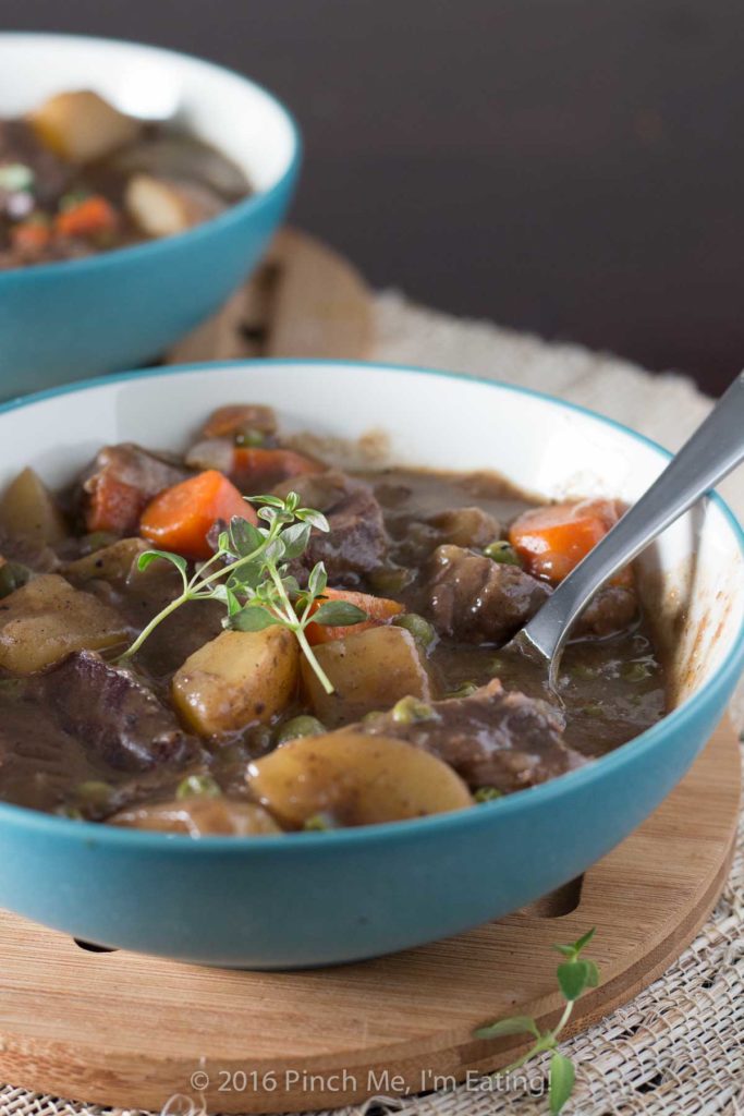 Close up side view of stove top beef stew with red wine in blue bowl with sprig of thyme