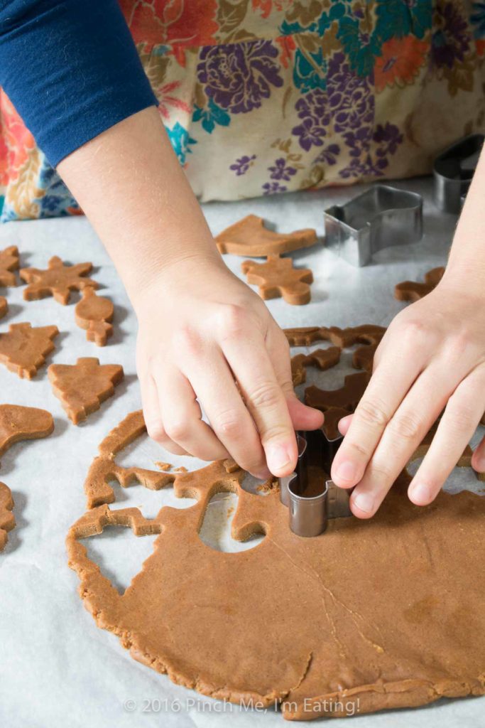 Woman in vintage flowered apron cutting out shapes for chewy gingerbread cookies with cookie cutters