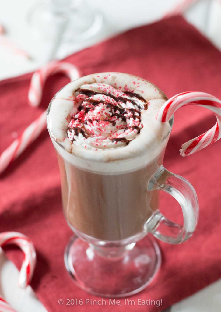 Mocha de hortelã-pimenta em caneca de vidro transparente com chantilly e bengalas doces em guardanapo vermelho