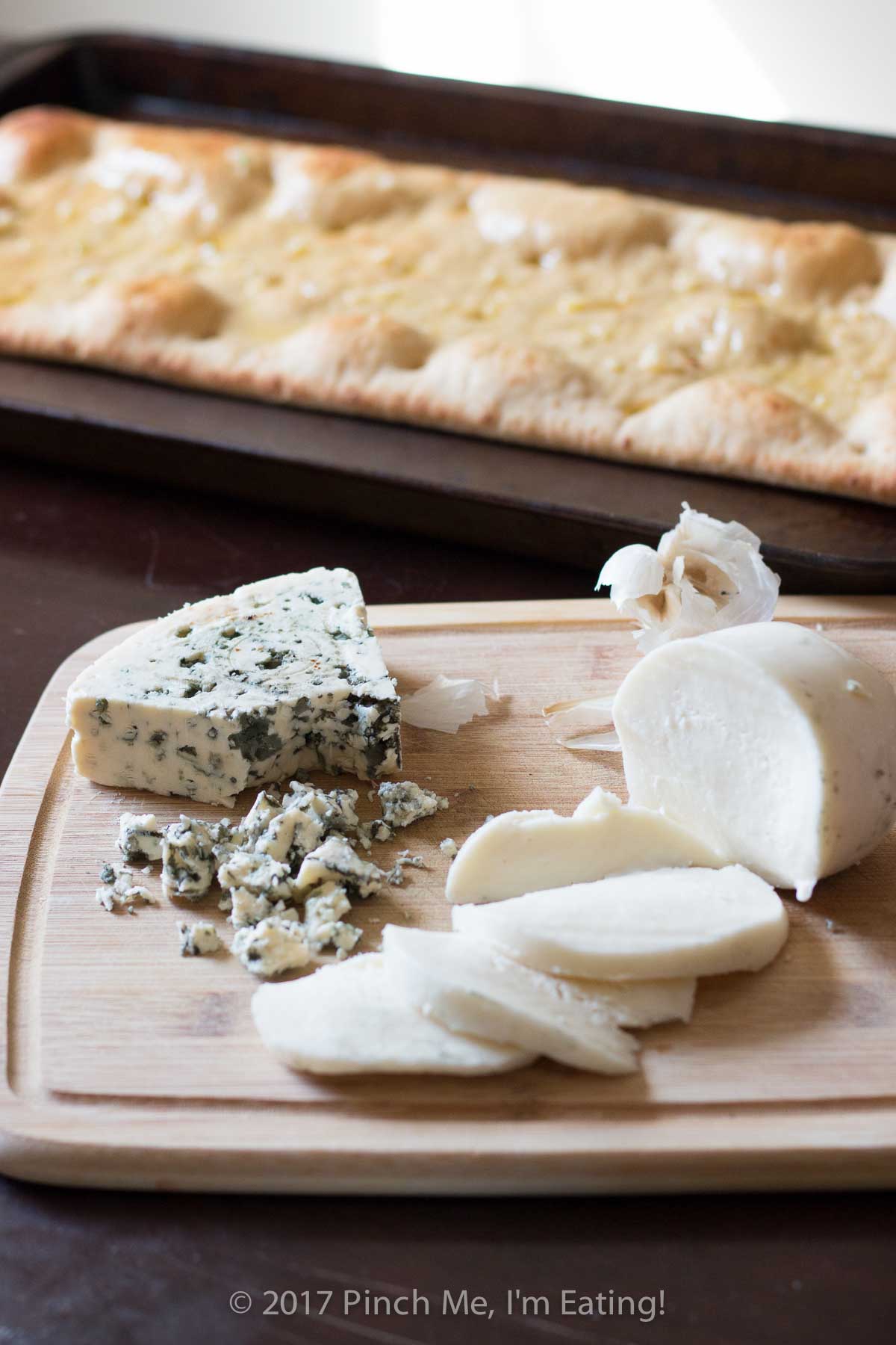 Blue cheese wedge and crumbles and fresh mozzarella cheese on a cutting board.