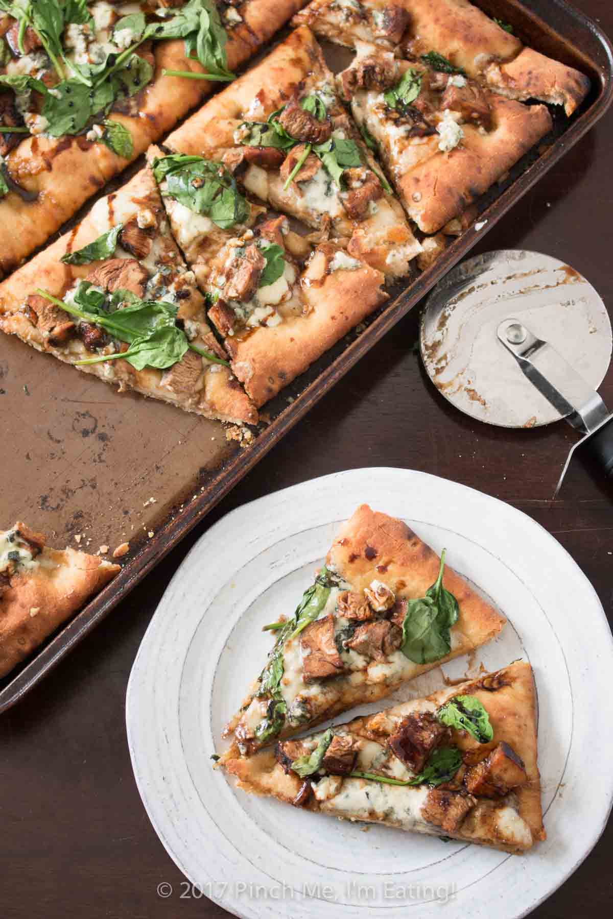 Balsamic chicken flatbread pizza on a baking sheet with two slices on a white plate.
