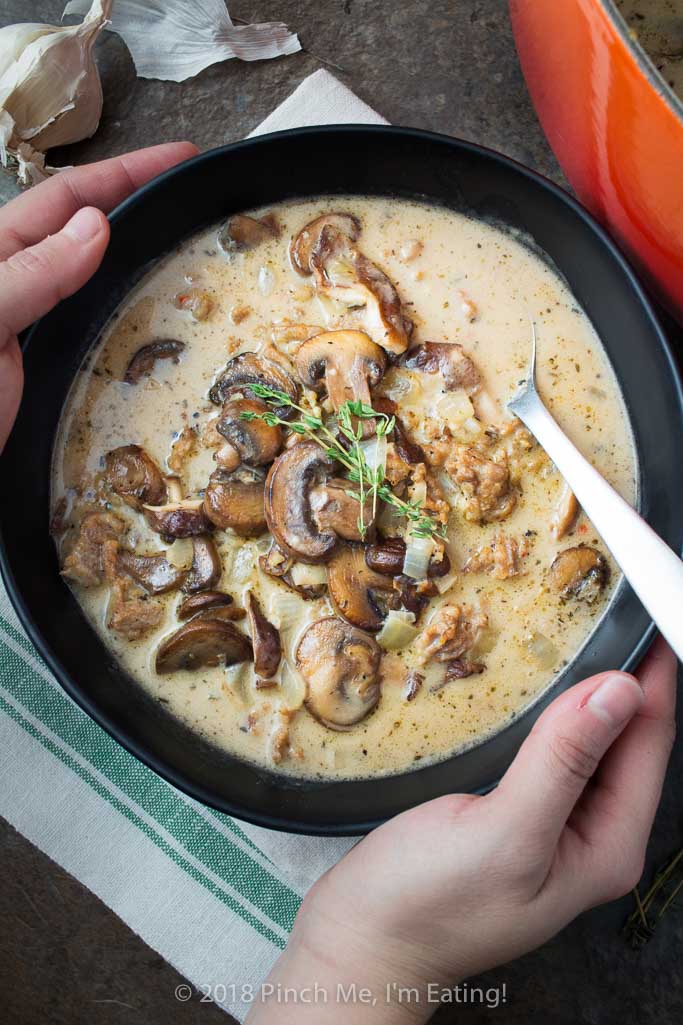 Overhead view of hands holding black bowl of creamy mushroom soup with Italian sausage