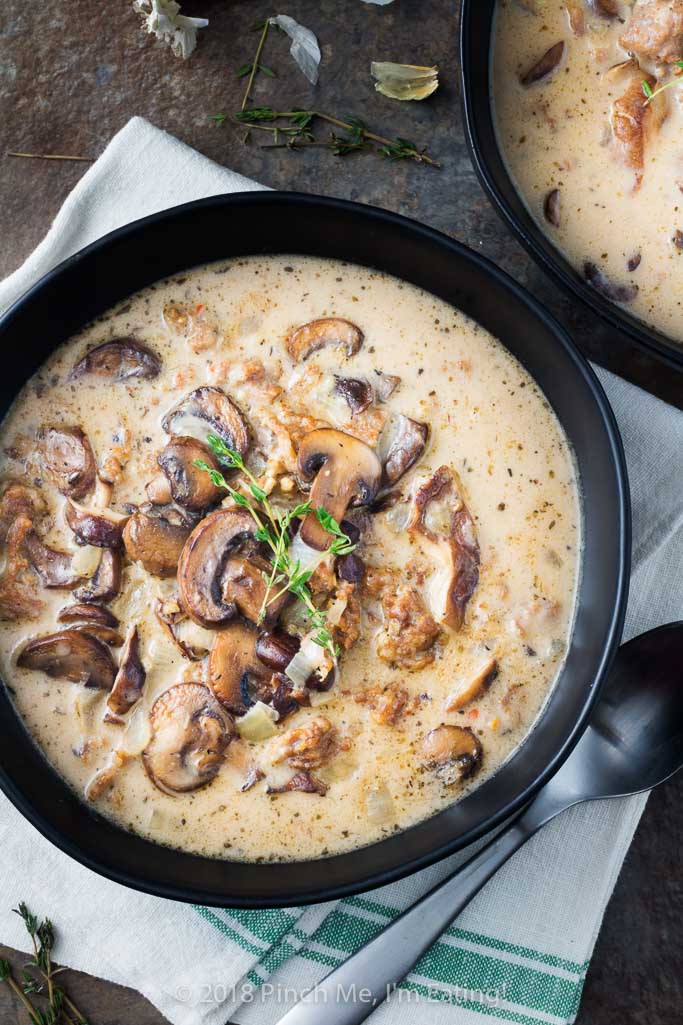 Overhead view creamy mushroom soup with Italian sausage in black bowl with sprig of thyme
