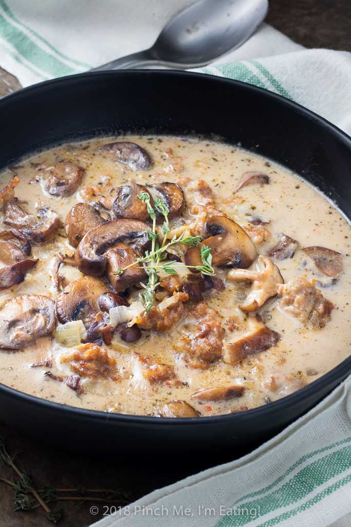 Three quarter view of creamy mushroom soup with Italian sausage in black bowl with sprig of fresh thyme