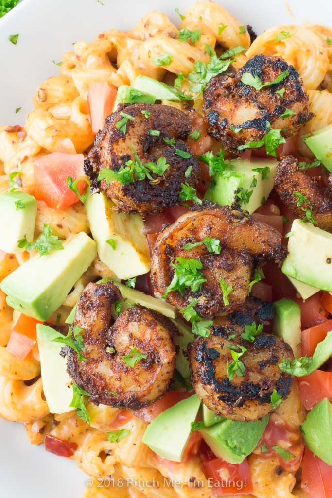 Closeup shot of chipotle macaroni and cheese with blackened shrimp, tomato and avocado in white bowl