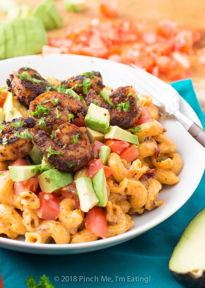 Three-quarter shot of chipotle mac and cheese with blackened shrimp, tomato and avocado in white bowl