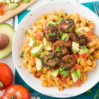 Overhead shot of chipotle mac and cheese with blackened shrimp in white bowl with tomatoes and avocado