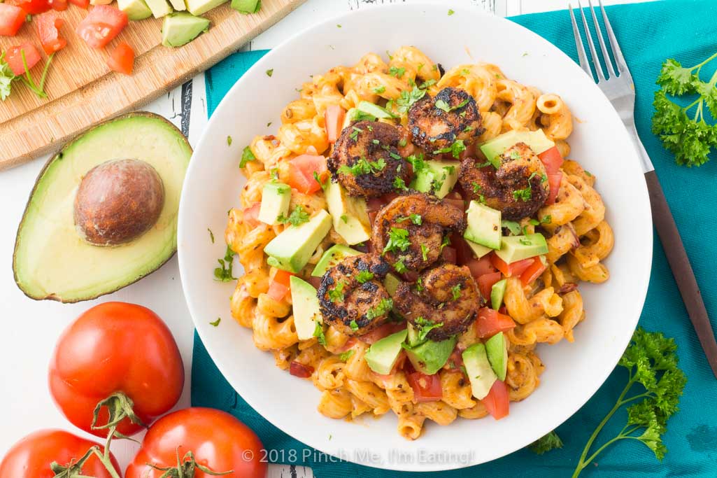 Overhead shot of chipotle mac and cheese with blackened shrimp in white bowl with tomatoes and avocado