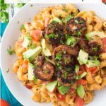 Overhead shot of chipotle mac and cheese with blackened shrimp in white bowl with tomatoes and avocado