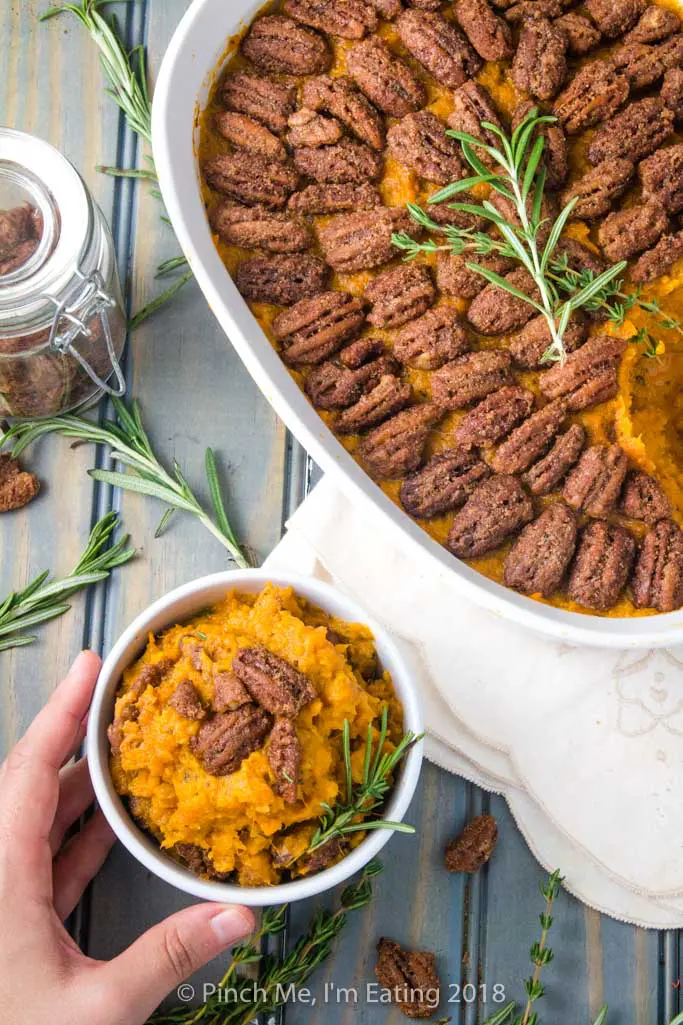 Overhead shot of sweet potato casserole with pecans in white serving dish and small white bowl, topped with rosemary