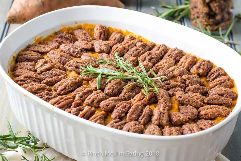 Sweet potato casserole with pecans candied in cinnamon sugar in white serving dish, topped with rosemary