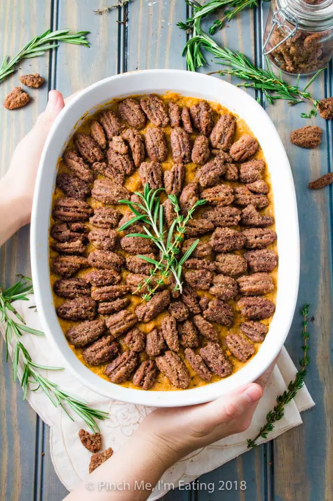 Overhead shot of sweet potato casserole with pecans candied in cinnamon sugar in white serving dish, topped with rosemary