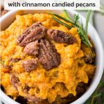 Mashed sweet potatoes in white bowl topped with candied pecans and rosemary