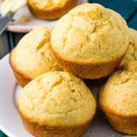 Five golden brown cornbread muffins stacked on a white plate