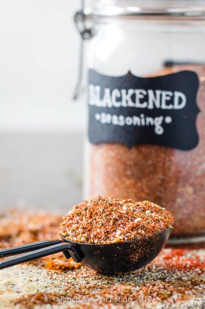 Closeup of blackened seasoning in measuring spoon with blurred spice jar in background