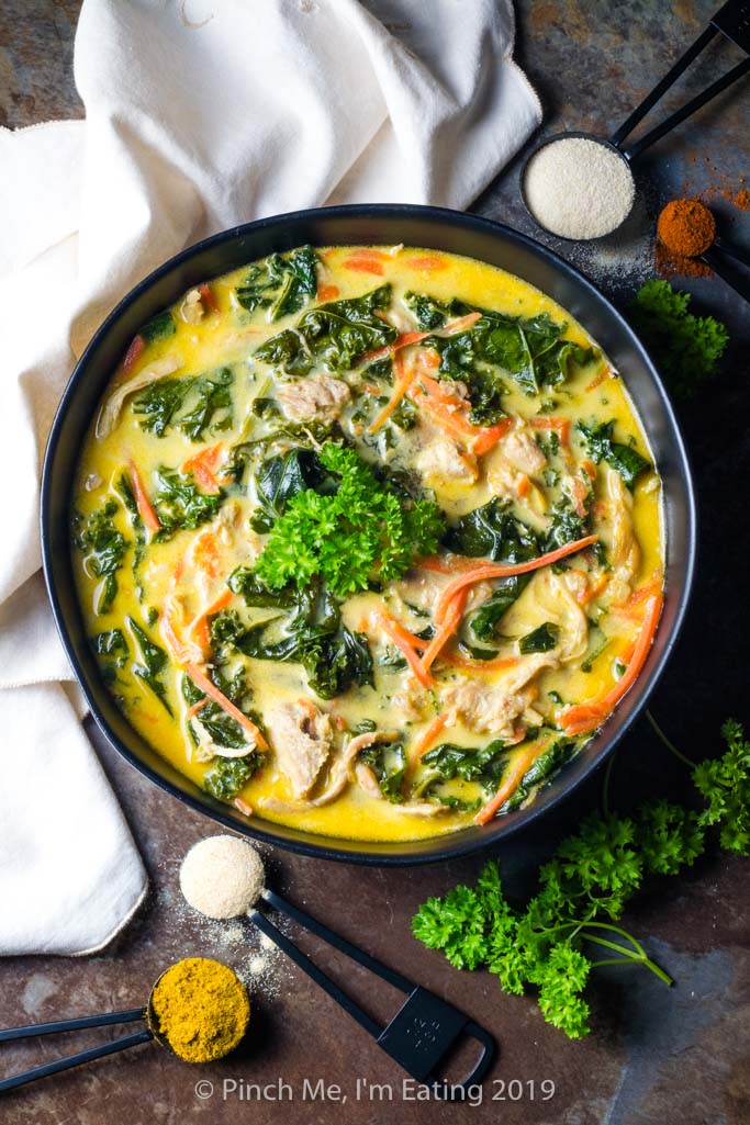 Overhead shot of coconut curry soup with chicken, carrots and kale, surrounded by spices