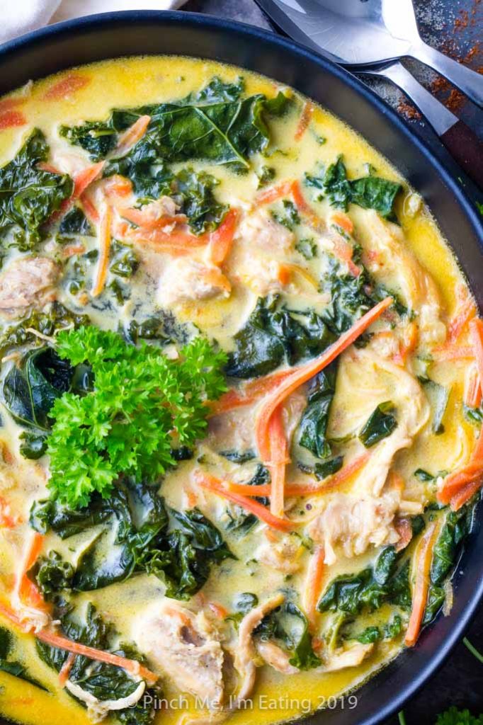 Closeup overhead shot of coconut curry soup with chicken, carrots and kale