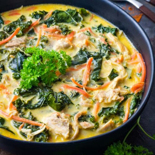 Three-quarter view of bowl of coconut curry chicken soup with carrots and kale