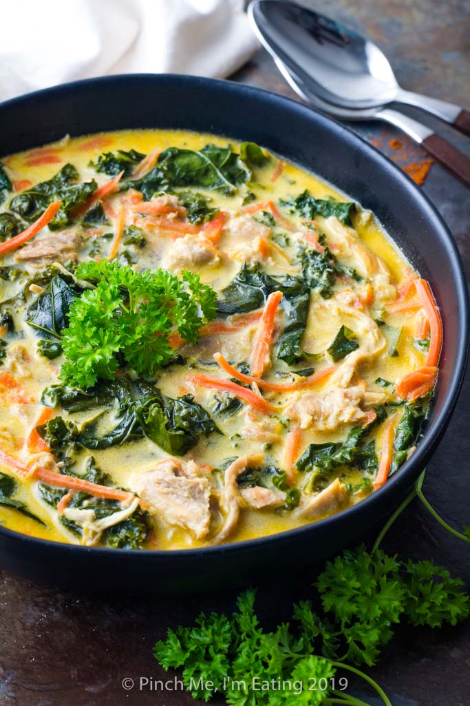 Three-quarter view of bowl of coconut curry soup with chicken, carrots and kale