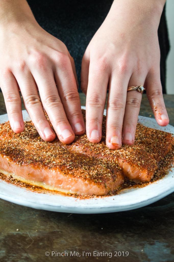 Patting blackening seasoning onto salmon fillets for blackened salmon