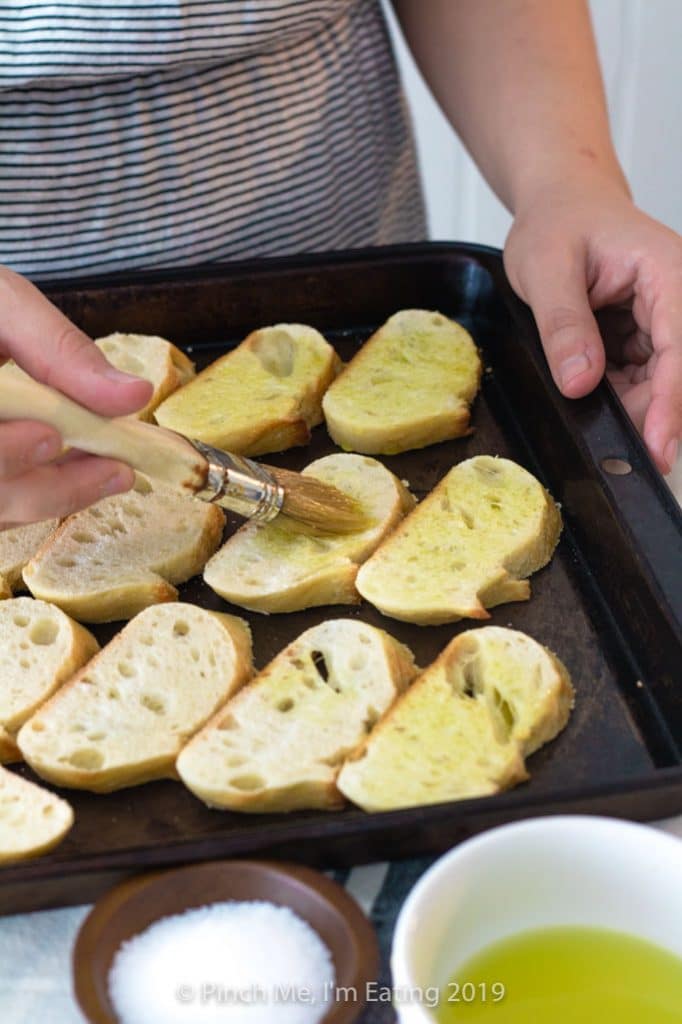 White woman brushing olive oil onto slices of bread to make crostini