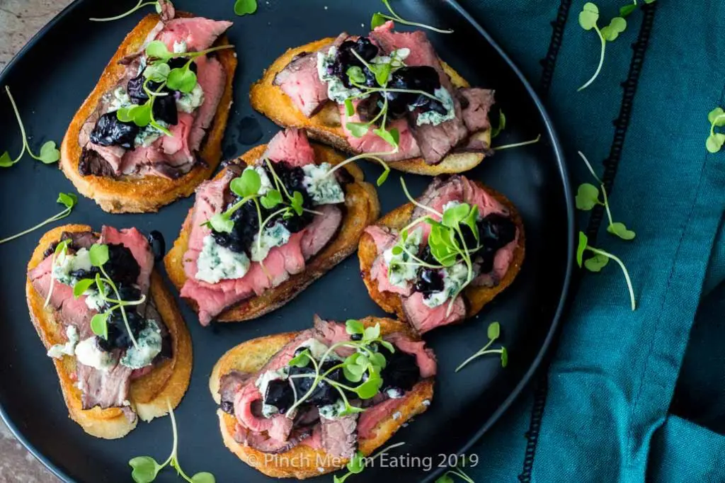 Flank steak crostini with blue cheese and blueberry caramelized onion jam and arugula microrgreens