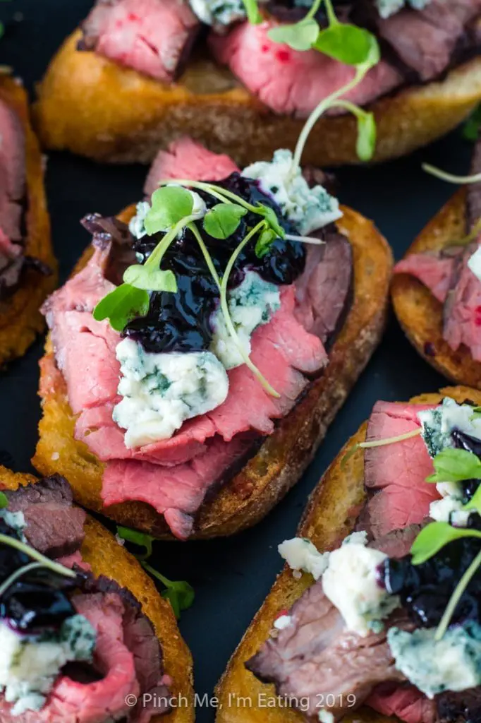 Medium rare flank steak crostini appetizers with blue cheese and blueberry caramelized onion jam and arugula microgreens