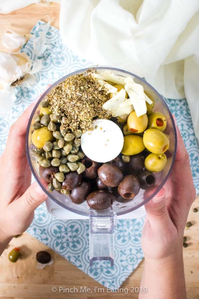 Black and green olives, capers, oregano, and garlic in a food processor