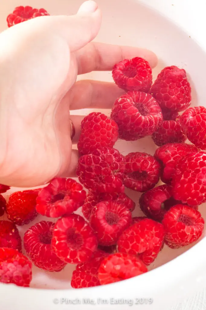 Raspberries being washed in a bowl of water