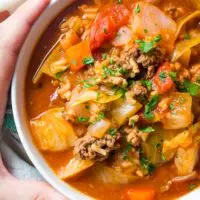 Bowl of unstuffed cabbage roll soup with hands around bowl