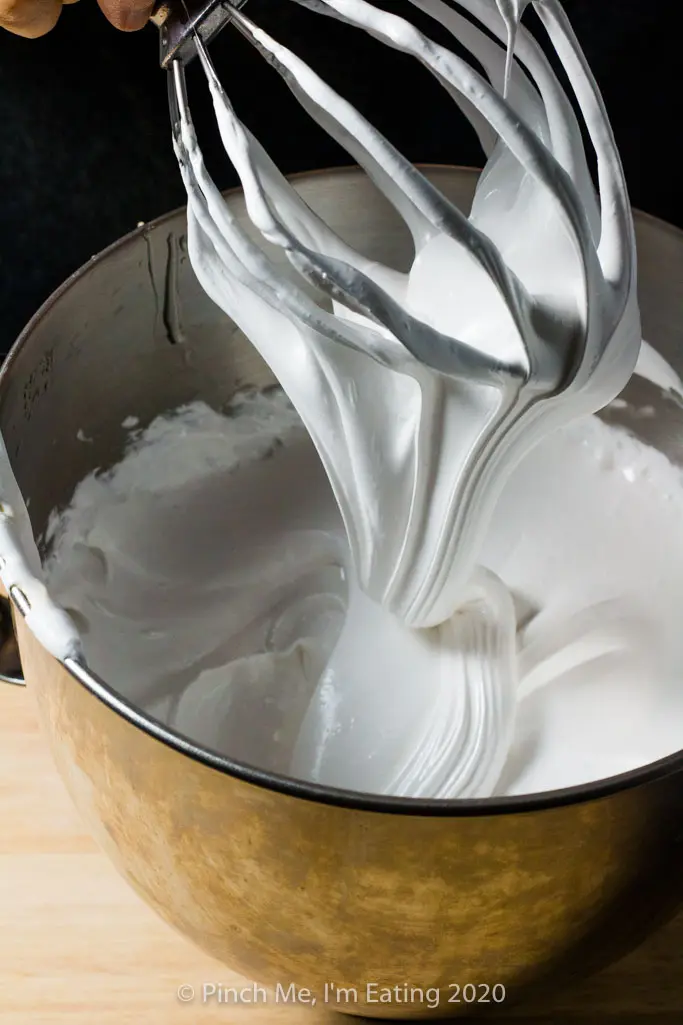 Homemade marshmallow mixture falls in a ribbon from a whisk attachment into a stainless steel bowl