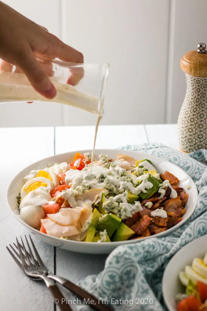 Turkey Cobb salad being drizzled with creamy blue cheese dressing