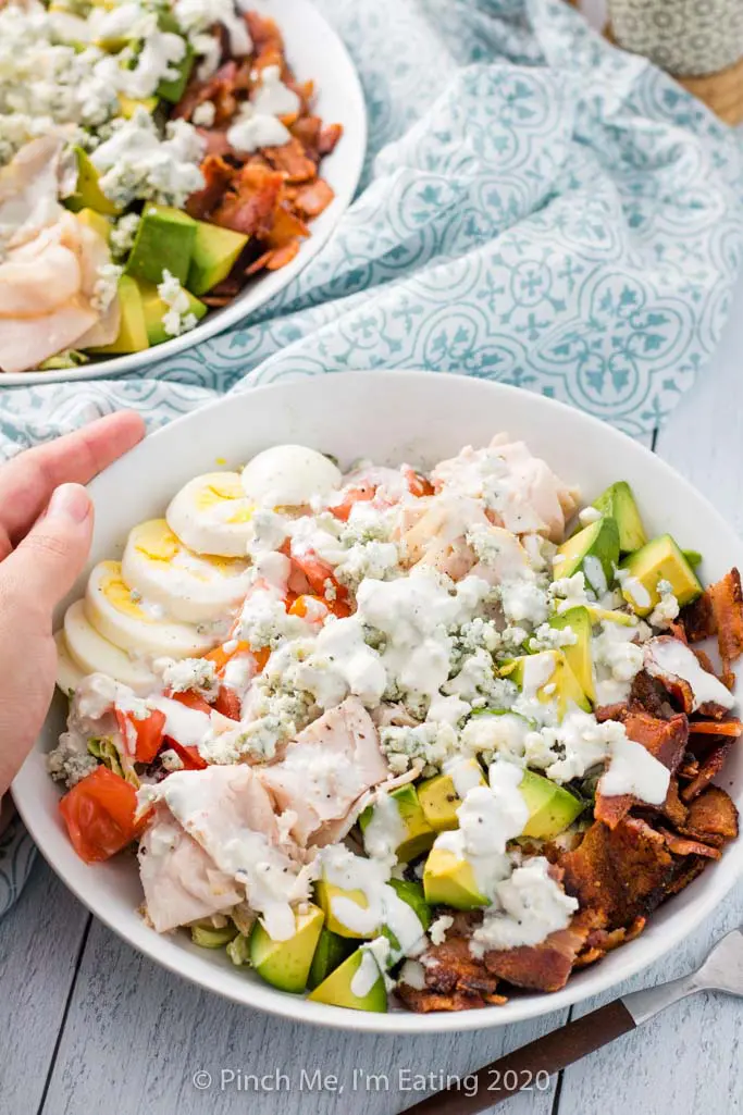 Overhead shot of turkey Cobb salad with bacon, avocado, turkey, blue cheese, tomato, and hard boiled egg in a white dish