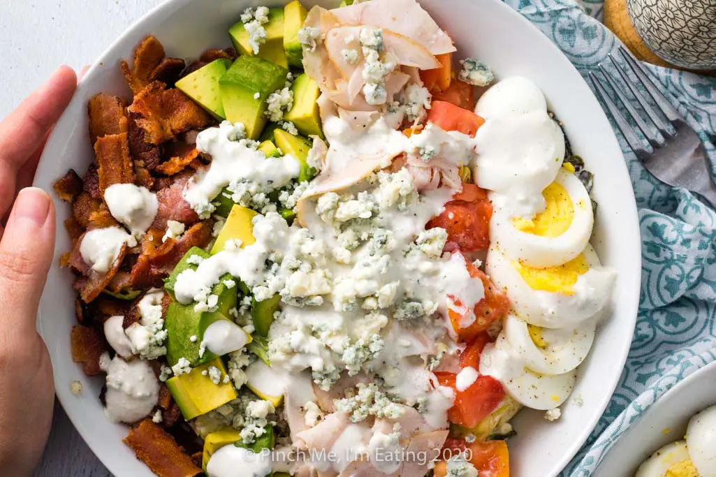 Hand on white dish of turkey Cobb salad