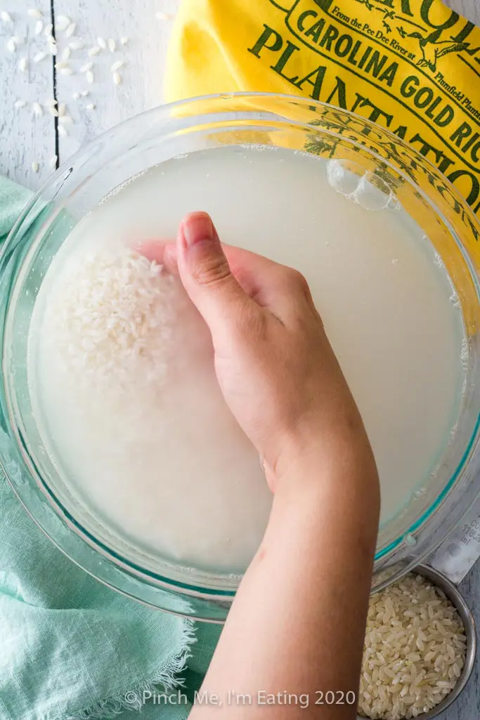 A hand gently swirls Carolina Gold rice in a bowl of water