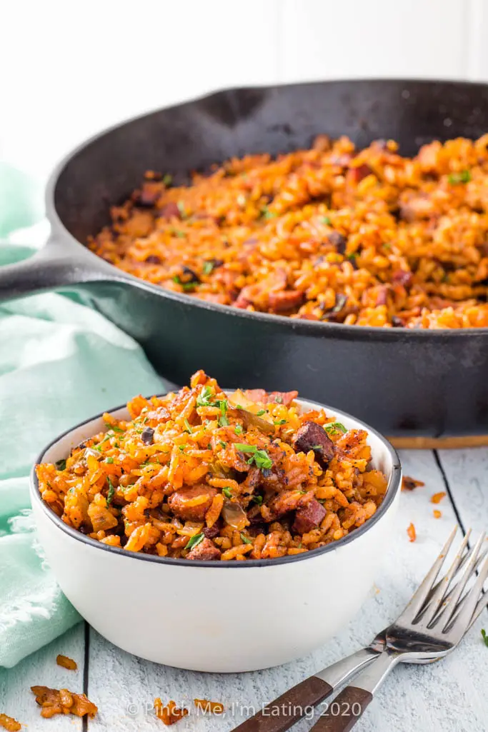A small bowl of Charleston red rice with sausage with two forks in front of a cast iron skillet
